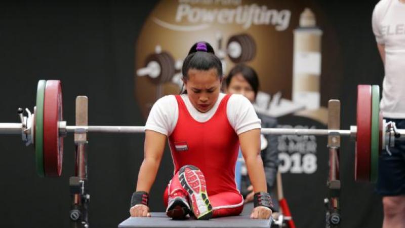 Woman bows head as she sits on powerlifting bench preparing to lift the bar